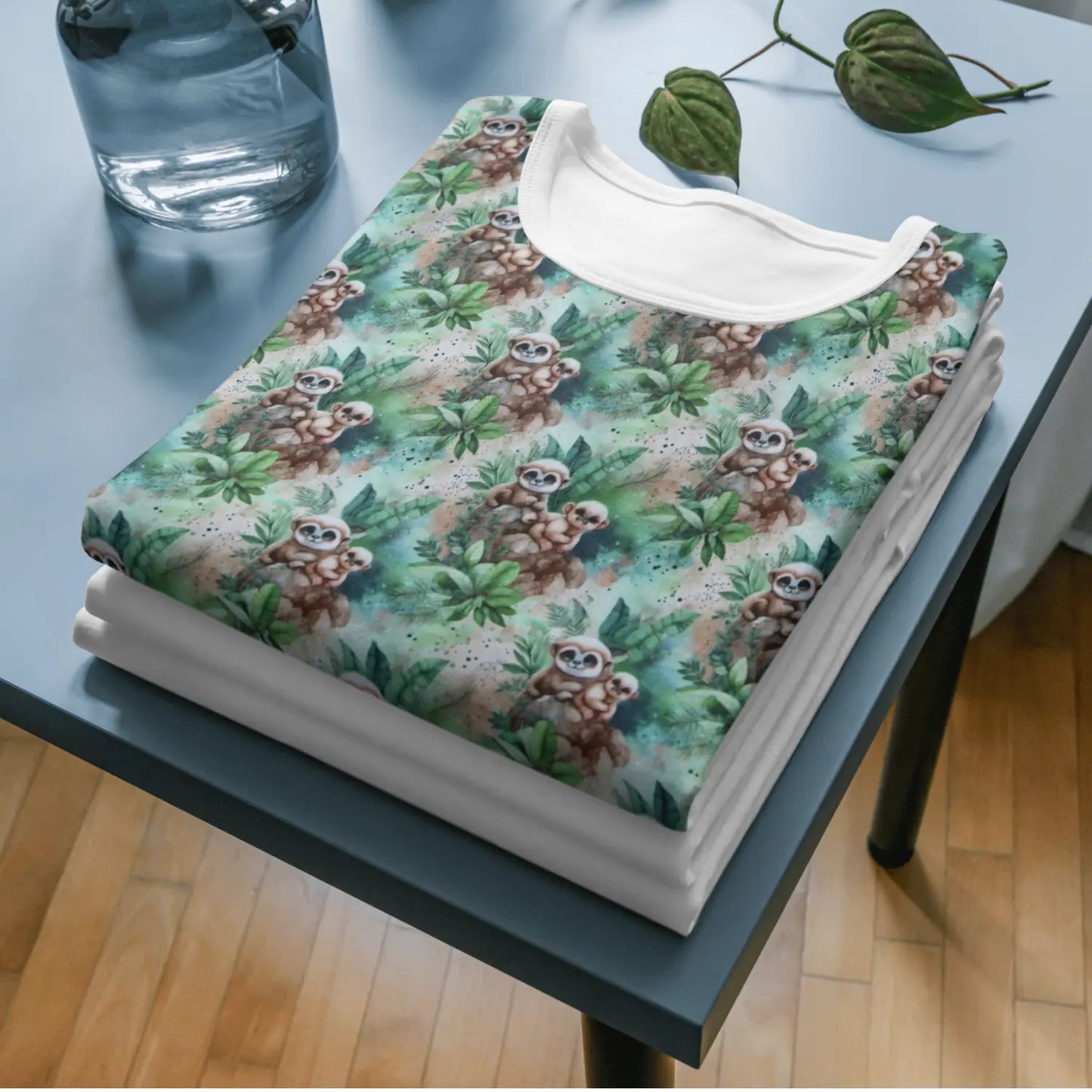 Beiger Baumwolljersey mit grünem Erdmännchen- und Blättermuster, auf weißem Stoff liegend.