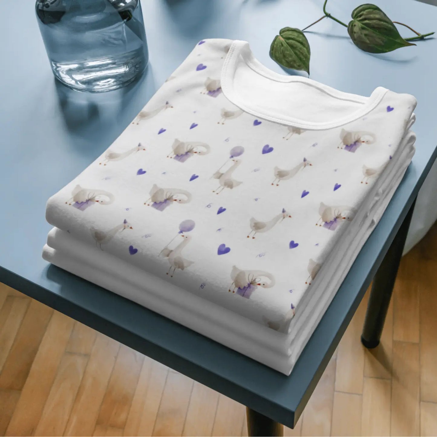 Weißer Baumwolljersey mit zarten lilafarbenen Vögeln und Sternen, gefaltet auf blauem Tisch.