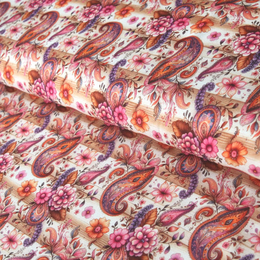 Baumwolljersey mit Paisleymuster in Braun und Rosa, rosa Blüten, auf Holzuntergrund drapiert.