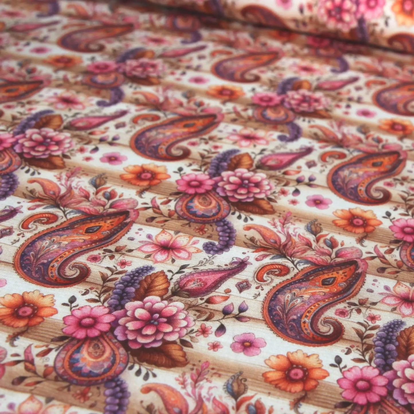Baumwolljersey Stoff mit rosa Blüten und braunen Paisleymustern auf hellem Hintergrund.