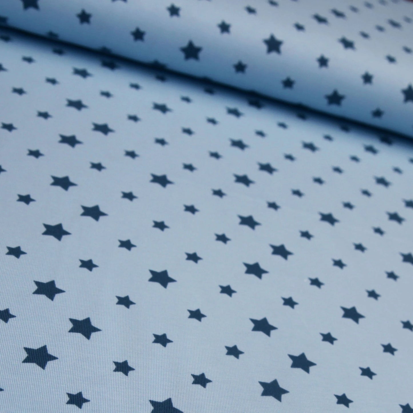 Babyblauer Baumwolljersey mit dunkelblauen Sternen in verschiedenen Größen.